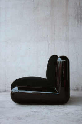 a black plastic chair standing in front of a concrete wall Logo Progressive Present