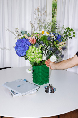 A green vase with flowers standing on a table Logo Progressive Present