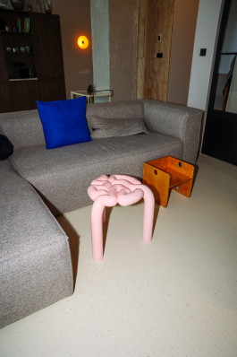 A pink stool standing in front of a grey couch Logo Progressive Present