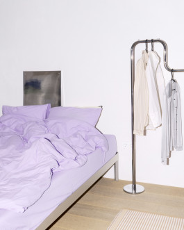 Clothing on a silver hanger standing next to a bed Logo Progressive Present