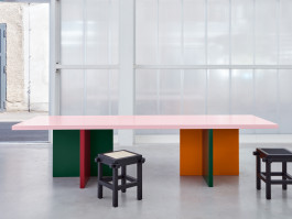 Tri-colored table standing in front of a plexiglass wall Logo Progressive Present