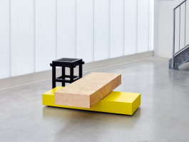 Wodden coffetable in brown and yellow colors standing in front of a plexiglas wall Logo Progressive Present