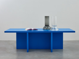 Blue table standing on a grey floor Logo Progressive Present