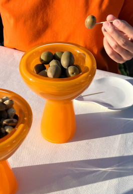 A orange glass vase holding some green olives. Logo Progressive Present