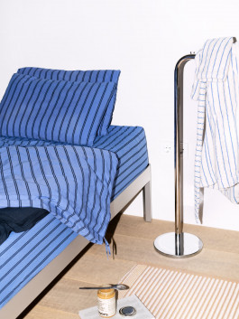Modern bedroom with blue striped bedding, minimalist metal bed frame, and chrome towel stand – Scandinavian-inspired interior design. Logo Progressive Present