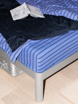 Close-up of a modern bed with blue striped bedding, navy blanket, and an open book – minimalist bedroom aesthetic. Logo Progressive Present