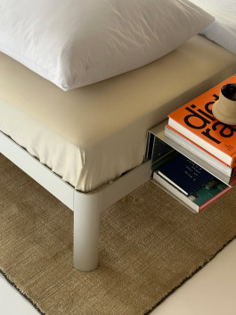 Modern bed with beige bedding and a minimalist floating nightstand holding books and a coffee cup – contemporary bedroom design. Logo Progressive Present