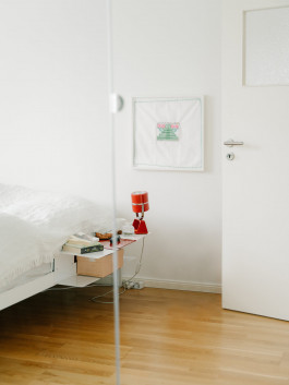Minimalist white bedroom with a floating bedside table, red lamp, and wooden flooring – modern Scandinavian interior design. Logo Progressive Present