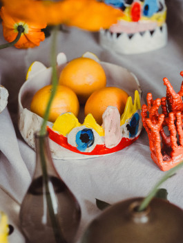 Handmade ceramic bowl with colorful whimsical face design holding fresh oranges, artistic table decor Logo Progressive Present