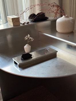 Minimalist steel table with sculptural incense holder, ceramic vase, and natural dried flowers in soft daylight Logo Progressive Present