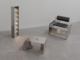 Minimalist interior with stainless steel lounge chair, sculptural rock-supported table, and geometric floor lamp with warm lighting Logo Progressive Present