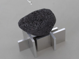 Black porous volcanic stone resting on a geometric aluminum base, with a drop of water falling above Logo Progressive Present