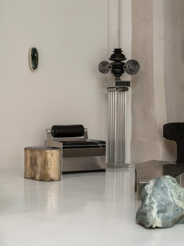 Modern interior with brushed steel lounge chair, sculptural lighting column, stone side table, and mixed material furniture Logo Progressive Present