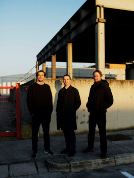 Three designers standing in front of a concrete structure in late afternoon light Logo Progressive Present