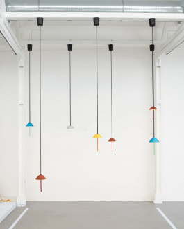 Minimal pendant lights in primary colors suspended from black cords in a white industrial ceiling Logo Progressive Present