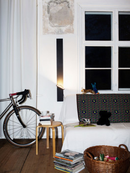 Vertical wall lamp in a lived-in interior with books, a bike, and toys Logo Progressive Present