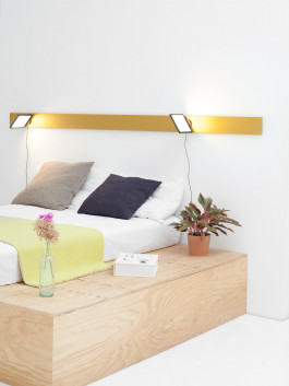 Minimalist bedroom with long yellow wall light above bed Logo Progressive Present