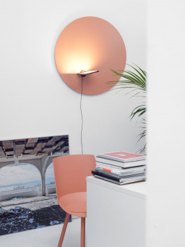 Circular wall light in warm terracotta tone above a coral chair and white desk in a contemporary interior Logo Progressive Present
