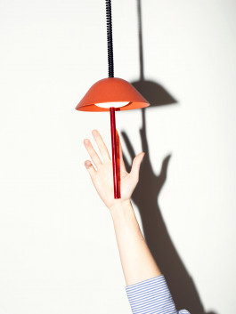 Hand reaching toward a red pendant light against a white wall Logo Progressive Present