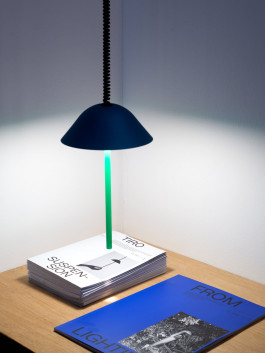 Pendant light in blue and green illuminating a stack of FROM LIGHTING booklets Logo Progressive Present