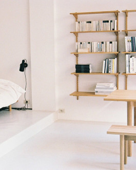 Wall-mounted wooden bookshelf and bench dining table in a bright minimalist room. Logo Progressive Present