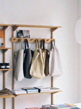Neutral-toned tote bags hanging on a wooden shelf in a minimal store interior. Logo Progressive Present