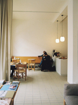 Cozy café interior with wooden furniture, pendant lights, and guests enjoying coffee. Logo Progressive Present