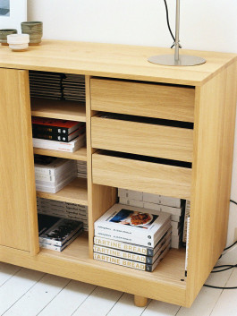 Light oak cabinet with books, magazines, and a metal desk lamp on top. Logo Progressive Present