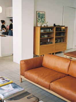 Brown leather sofa and glass-fronted wooden cabinet with ceramic dishes. Logo Progressive Present