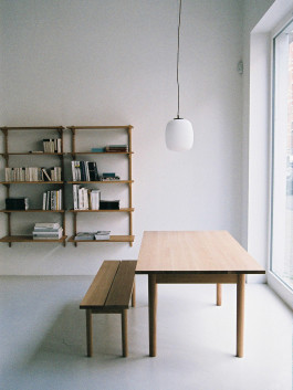 Minimal wooden dining table with bench and wall-mounted bookshelves. Logo Progressive Present