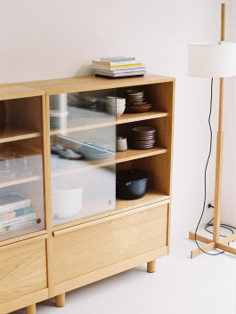 Wooden sideboard with sliding glass doors and neatly stacked ceramic dishes. Logo Progressive Present