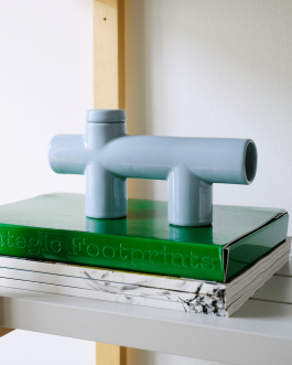 Light blue ceramic object with sculptural, pipe-like shapes placed on a green book titled 