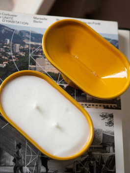 Two oval ceramic trays in yellow, one used as a candle vessel, placed on a Le Corbusier architecture book. Logo Progressive Present