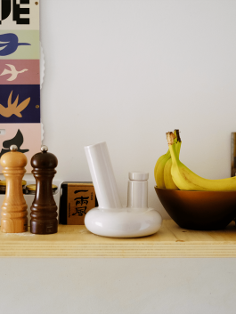 White ceramic pipe on a wooden kitchen shelf next to bananas and spice grinders. Logo Progressive Present
