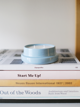 Sky-blue ceramic candle on a stack of architecture and design books. Logo Progressive Present