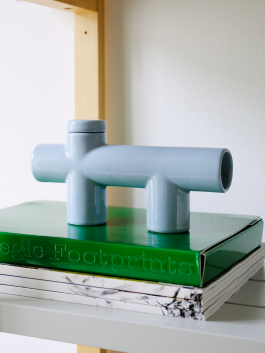 Sky-blue ceramic pipe with architectural form placed on a green book titled 