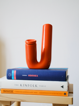 Bright orange ceramic pipe with a bold U-shape, placed on a stack of books. Logo Progressive Present