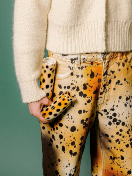 Person holding two leopard-patterned ceramic pipes while wearing splatter-dyed pants and a cream knit sweater. Logo Progressive Present