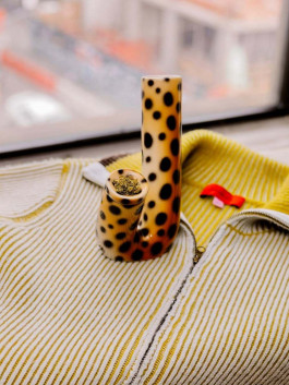 Ceramic smoking accessory with leopard pattern placed on a striped zip-up top. Logo Progressive Present