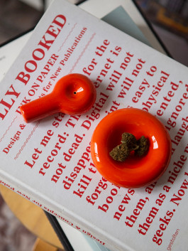 Red ceramic smoking set with a pipe and ashtray resting on a bold red-and-white book cover. Logo Progressive Present