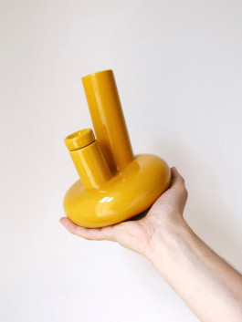 Yellow ceramic bong with sculptural shape, held in a person's hand against a neutral background. Logo Progressive Present
