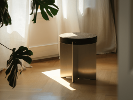 Round cork and aluminum side table bathed in natural light near a white curtain. Logo Progressive Present
