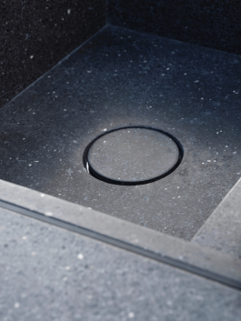 Close-up of a dark stone kitchen sink with integrated circular drain cover. Logo Progressive Present