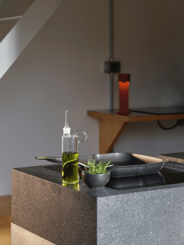 Detail view of a dark stone kitchen countertop with olive oil, rosemary, and a pan. Logo Progressive Present