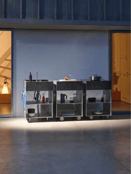 Outdoor modular kitchen setup at dusk with integrated lighting and open shelving. Logo Progressive Present